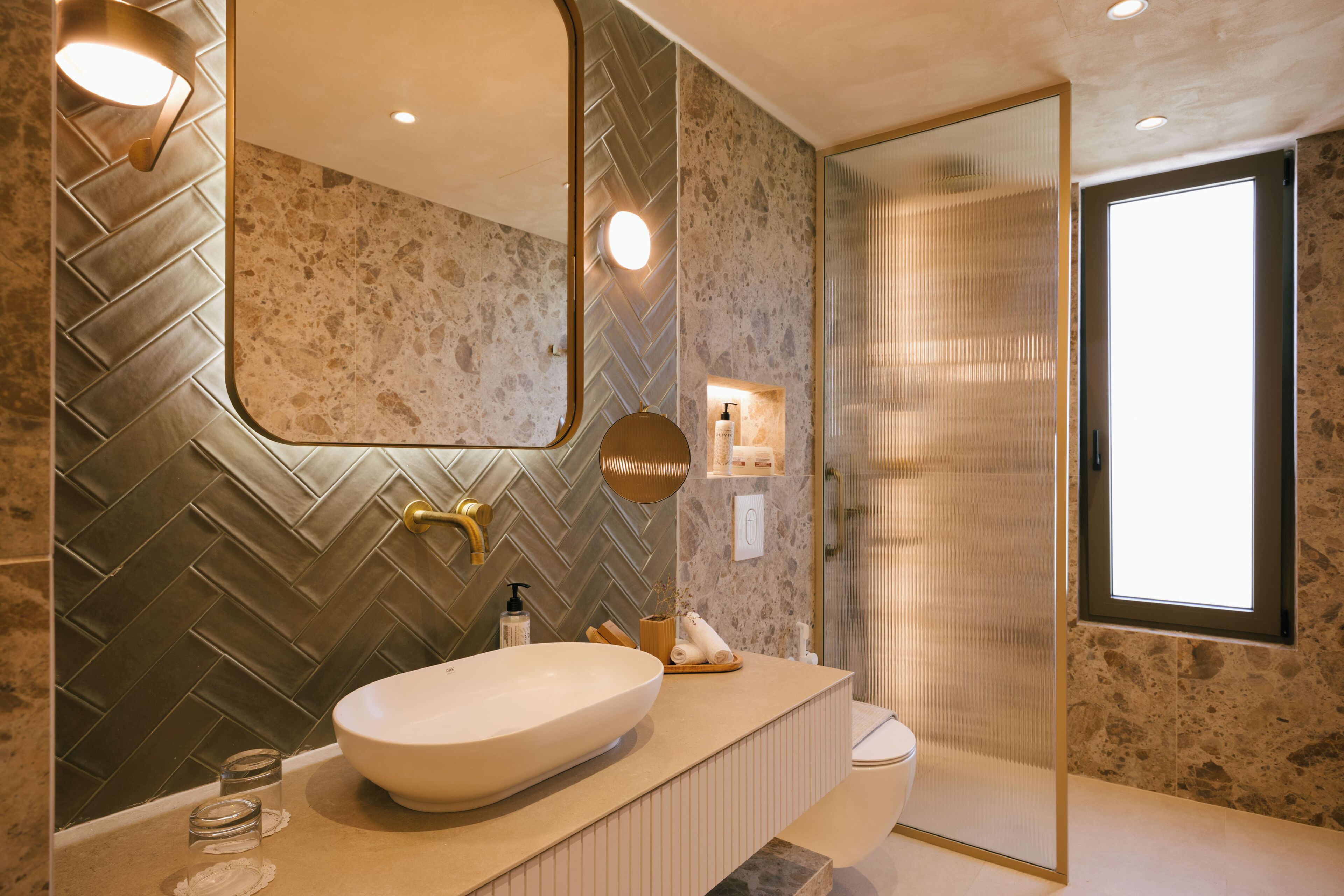 Un baño moderno con un espejo grande, un revestimiento de pared con diseño de espiga, una bañera independiente y un box de ducha de vidrio.