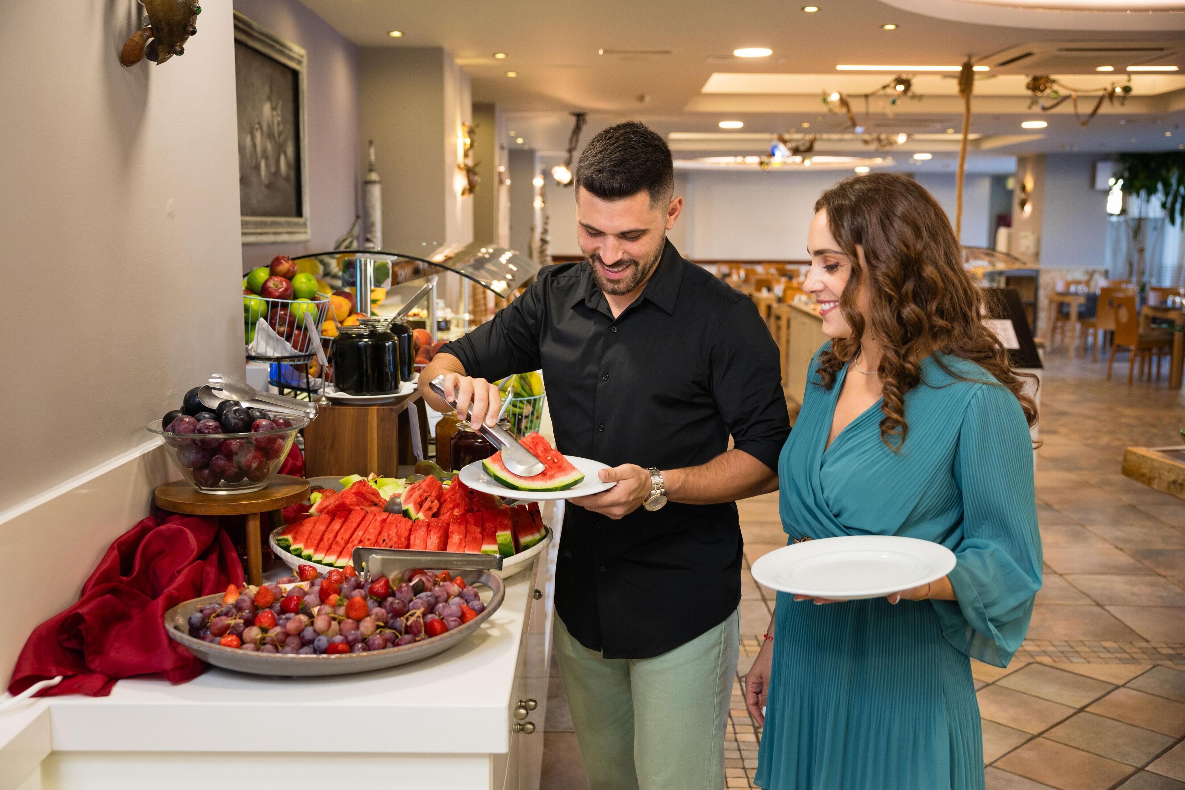 Un buffet garni de différents fruits, et un homme qui sert les plats.