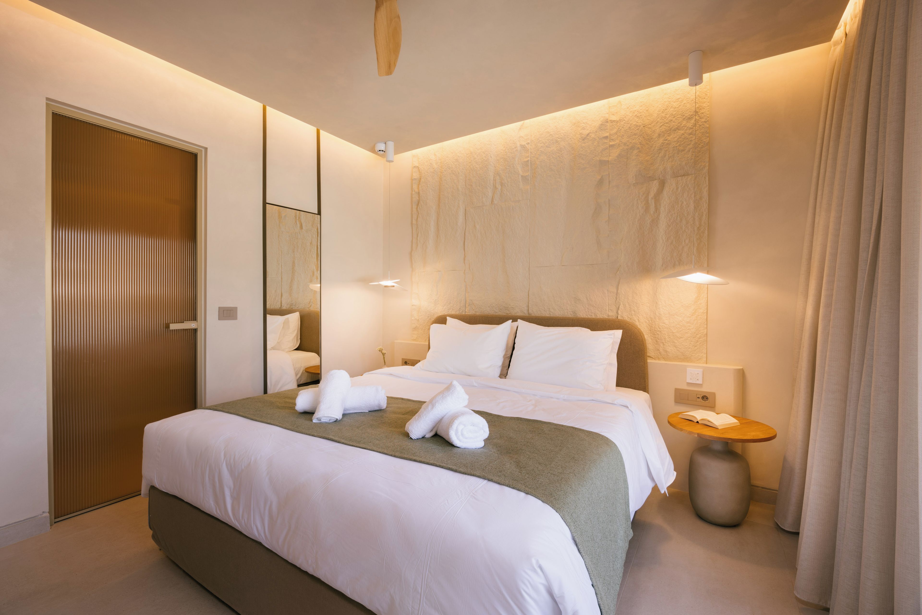 A hotel room with a large bed, a bedside table, a mirror, and a door.