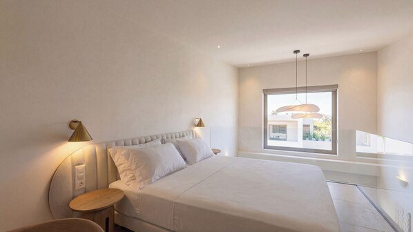 Un dormitorio moderno con una cama grande, una mesita de noche y una lámpara. Se ve una ventana con vistas a un edificio.