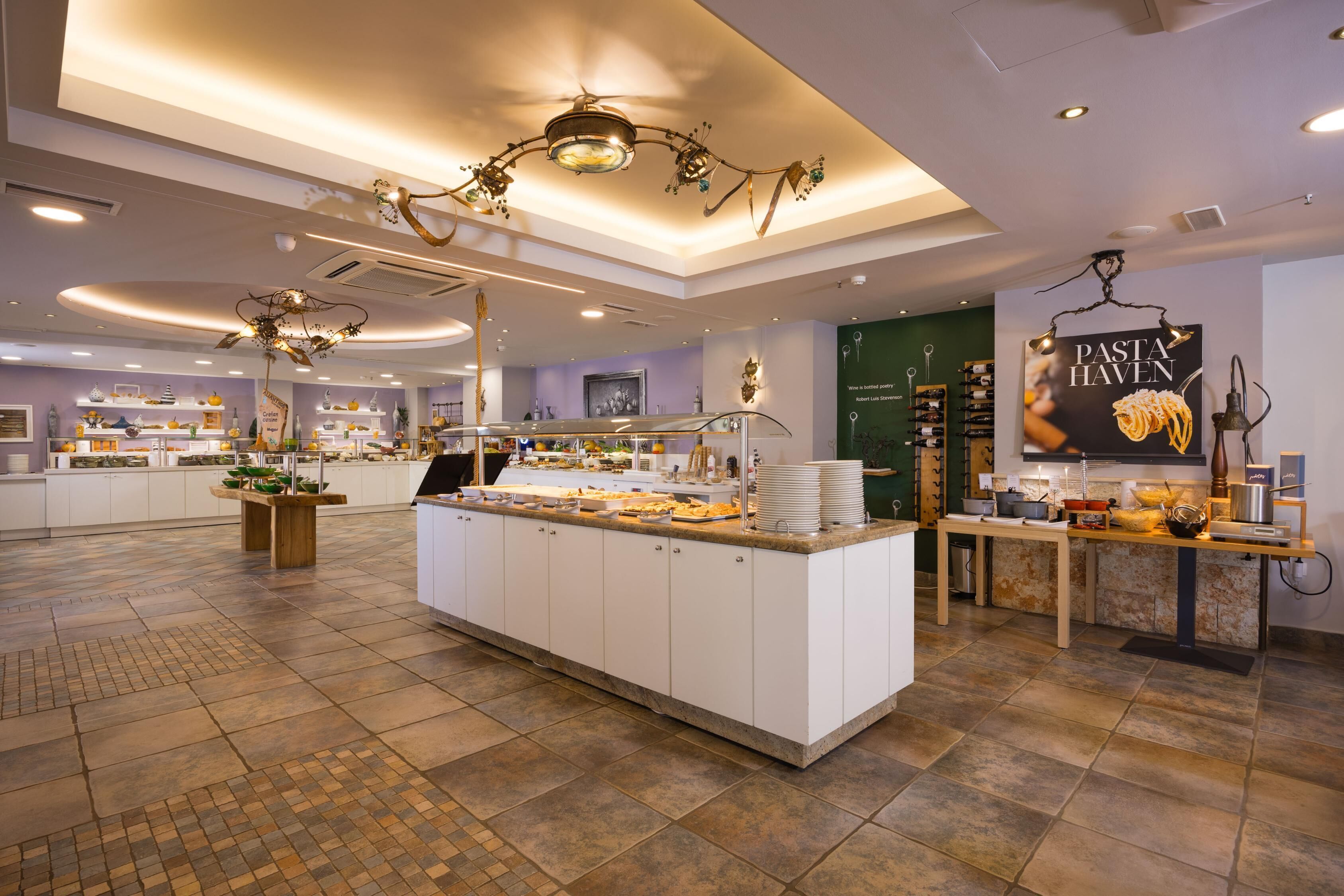A spacious hotel lobby with a central island featuring a buffet, surrounded by white cabinetry and a tiled floor.