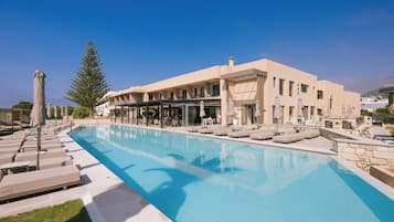 A poolside area with lounge chairs and umbrellas, a clear sky, and a building with multiple windows and balconies.