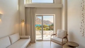 Ein modernes Zimmer mit einer Couch, einem Sessel und Meerblick durch eine Glastür.