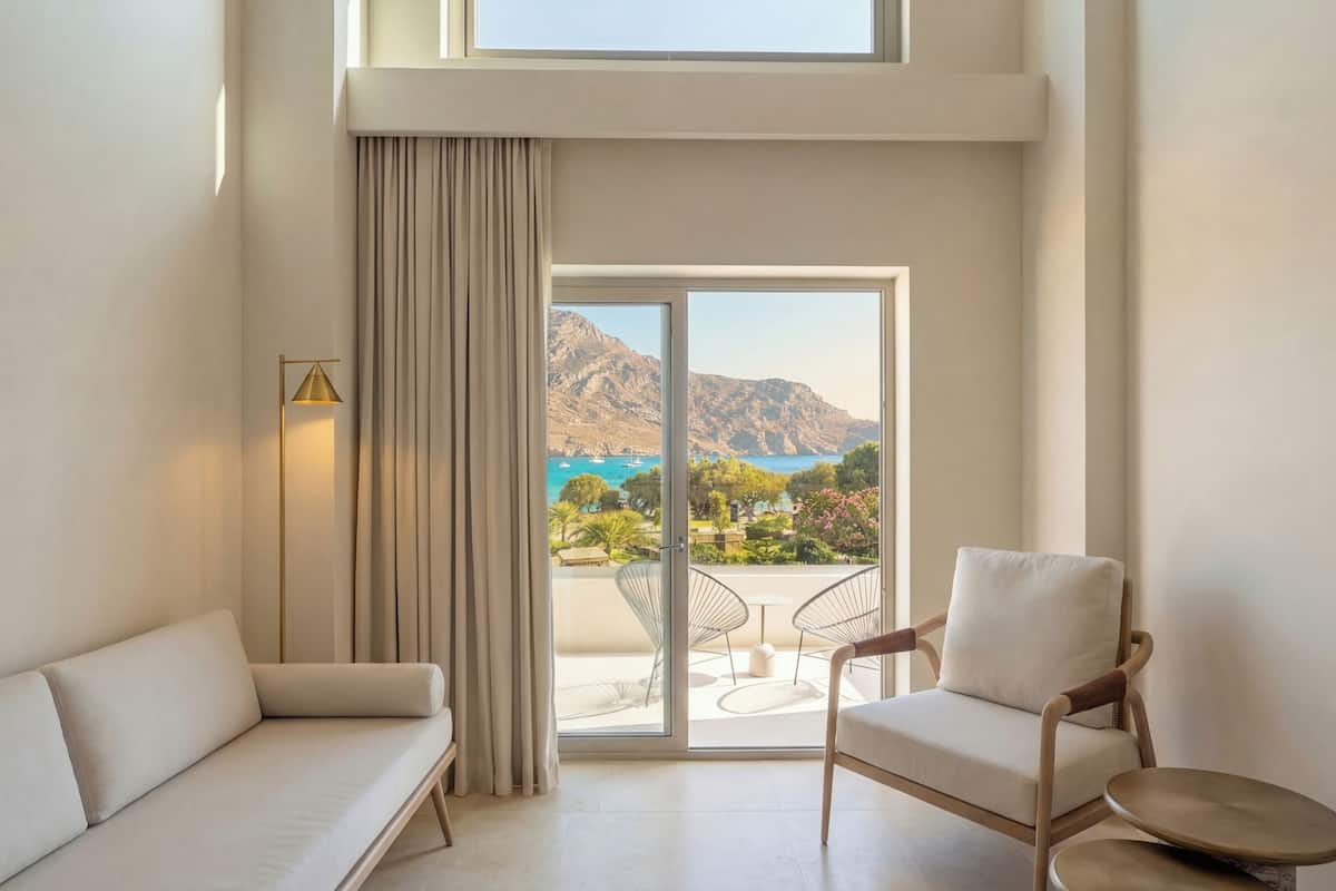 Habitació moderna amb un sofà, una cadira i vista al mar i a les muntanyes a través d'una gran porta corredissa.