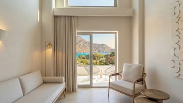 Una habitación moderna con sofá, sillón y vistas al mar y a las montañas a través de un amplio ventanal corredera.