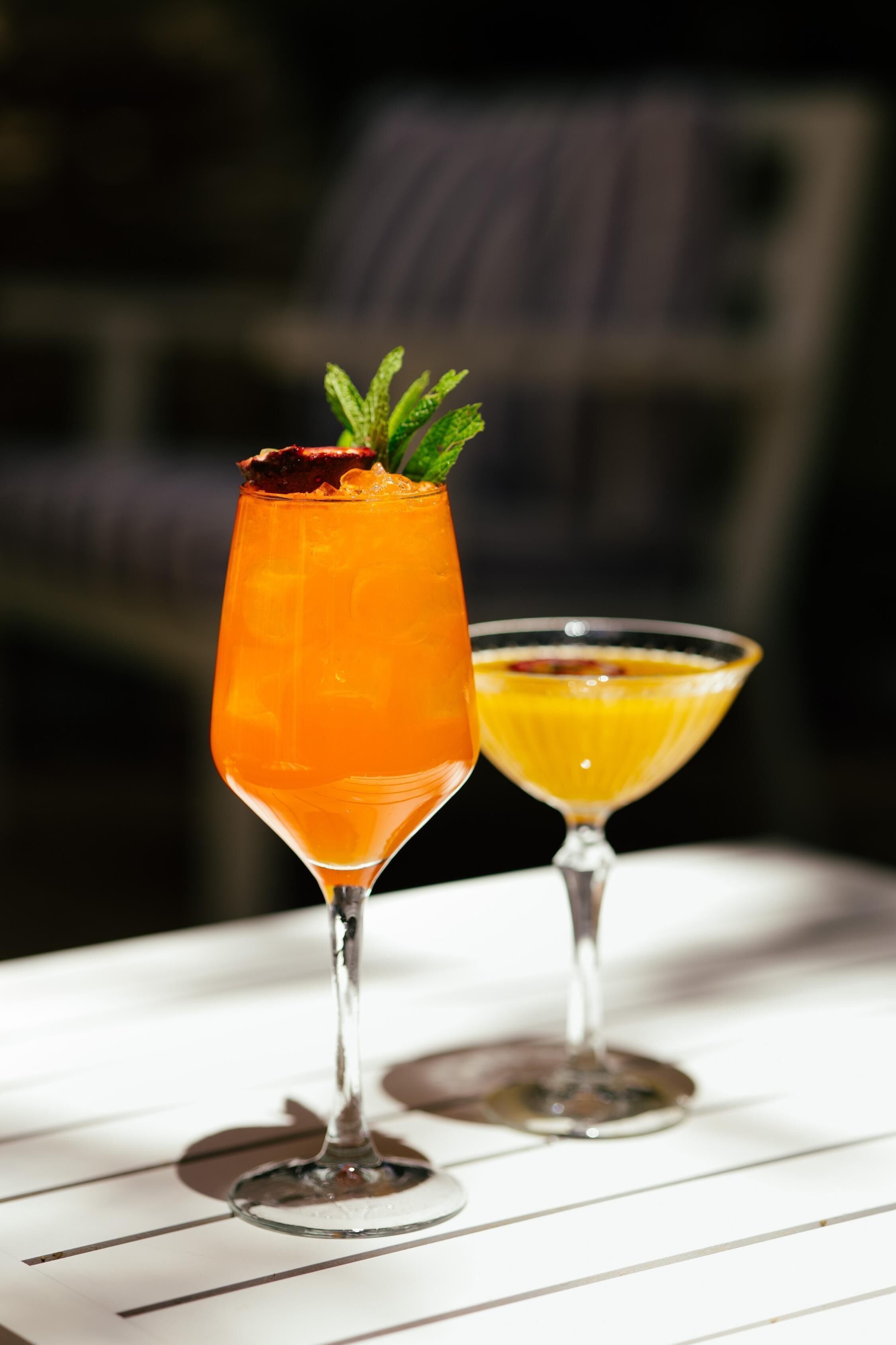 Two cocktails in martini glasses on a white table.