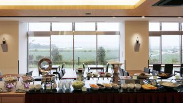 Ein Buffet mit verschiedenen Speisen und Blick auf eine grüne Landschaft durch große Fenster.