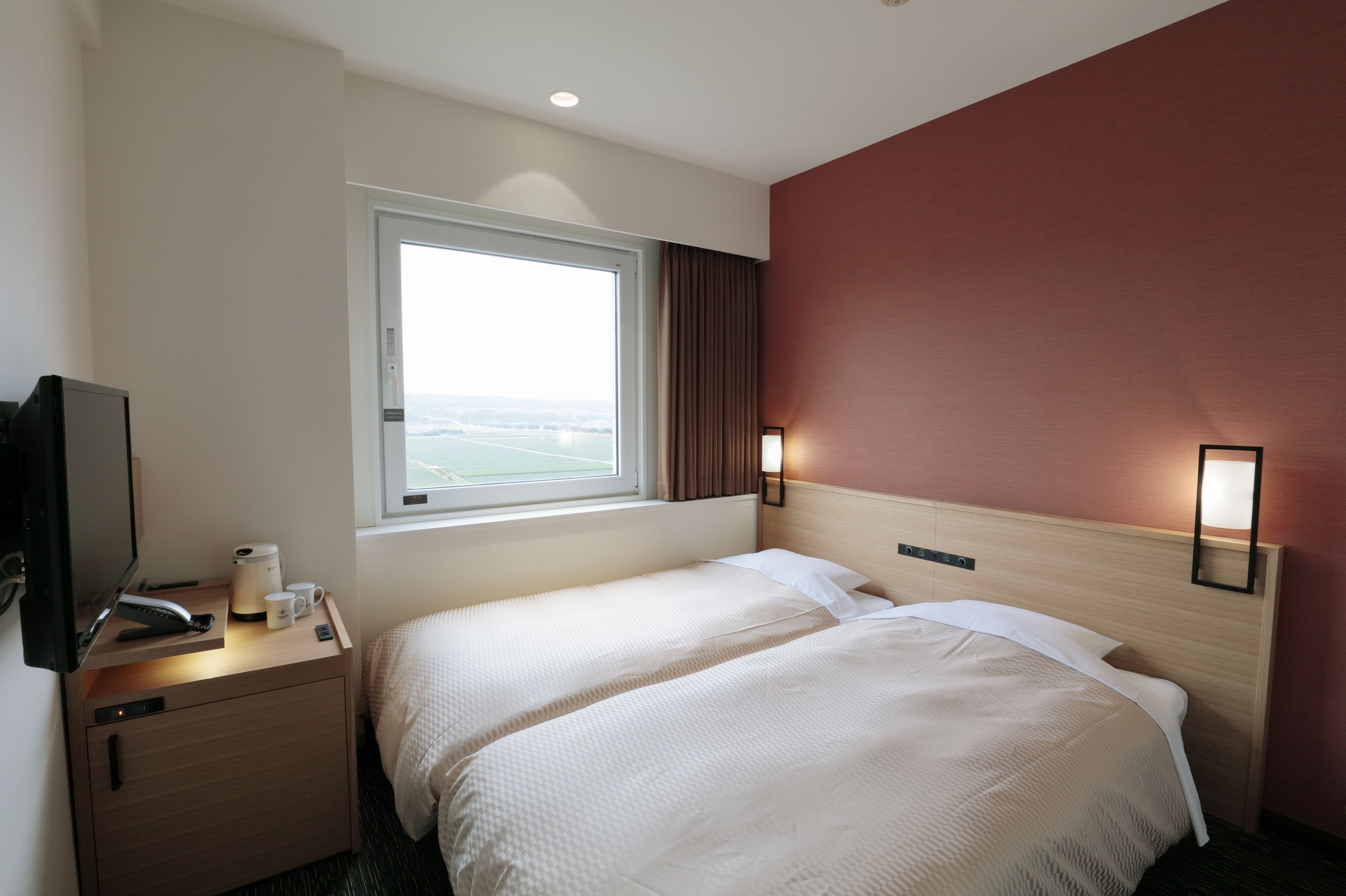 Habitación de hotel con dos camas, televisión, cafetera y ventana con vistas.