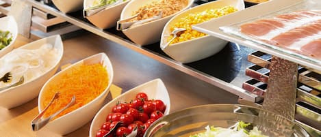 A buffet with various food items including vegetables, corn, and meat.
