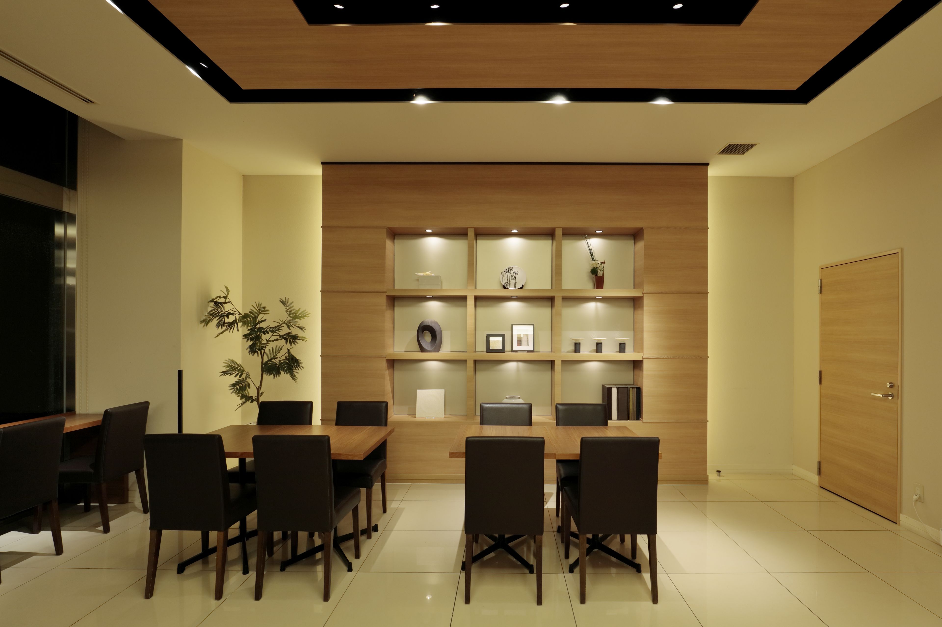 A modern dining area with a wooden table and chairs, a potted plant, and a wall-mounted shelf with decorative items.
