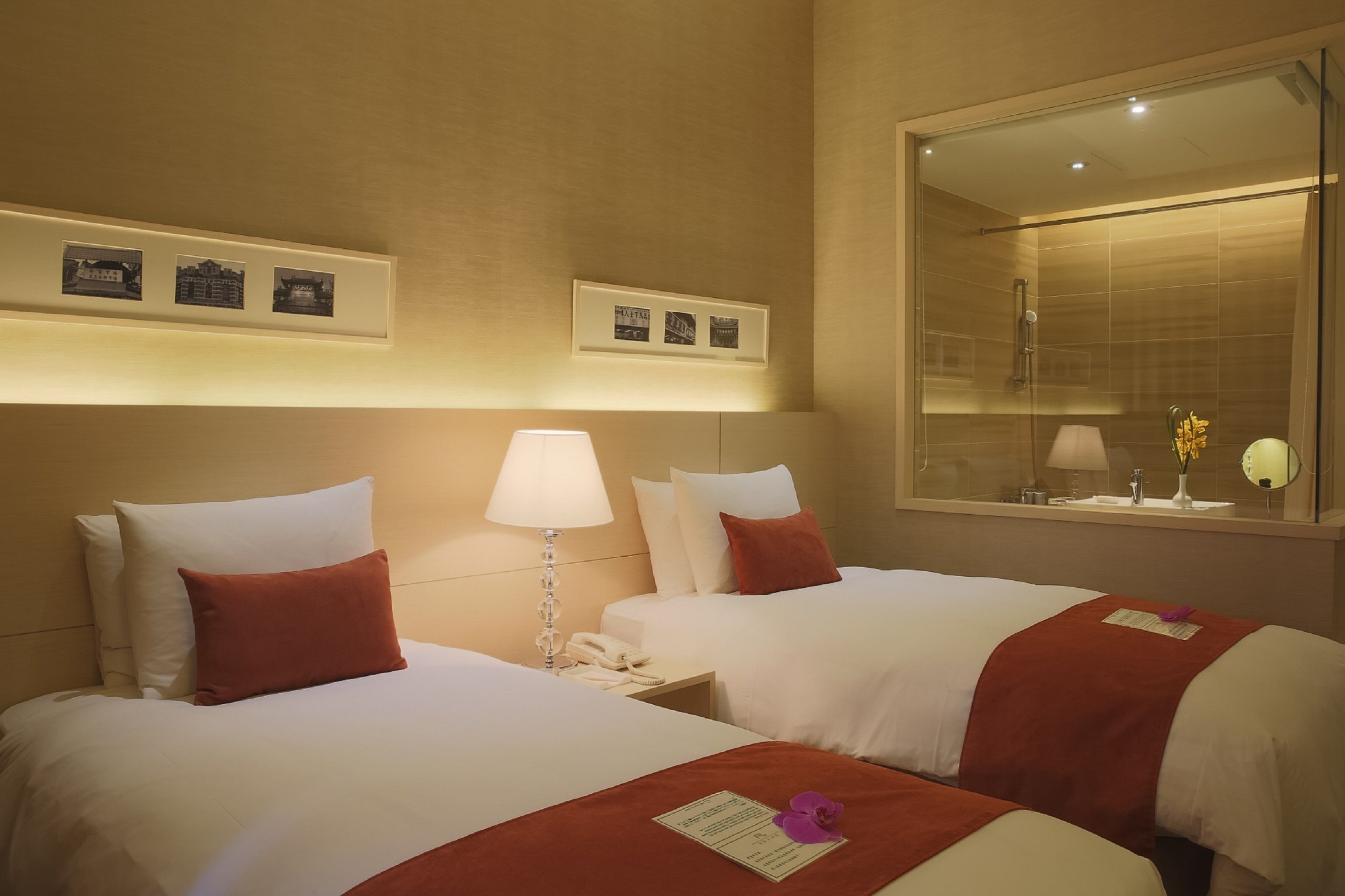 Una habitación de hotel con dos camas, una mesita de noche con lámpara, un espejo y cuadros en la pared.