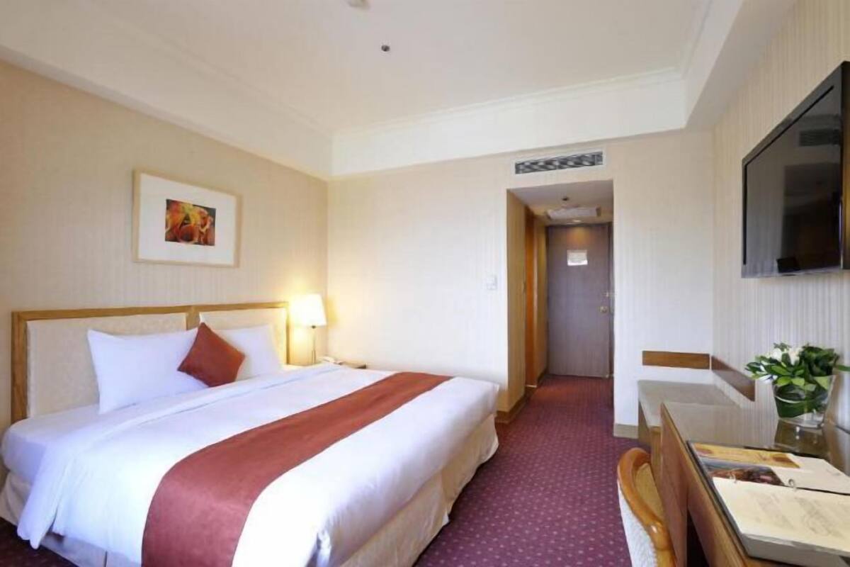 A hotel room with a large bed, a desk with a chair, a television, and a framed picture on the wall.