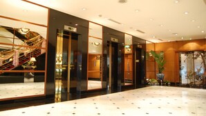A modern hotel lobby with a marble floor, a staircase with a golden railing, and a large potted plant. - Hotel Riverview Taipei (Taipei)