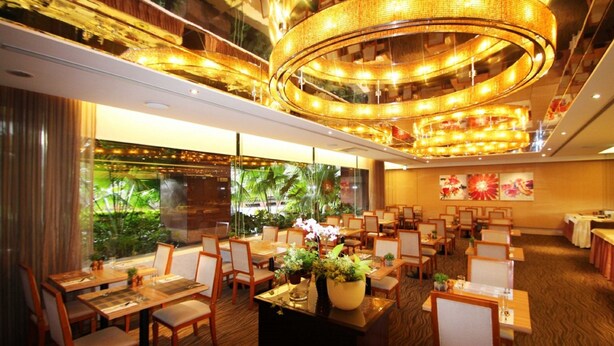A restaurant with multiple dining tables and chairs, a central decorative light fixture, and a view of greenery through large windows. - Hotel Riverview Taipei (Taipei)