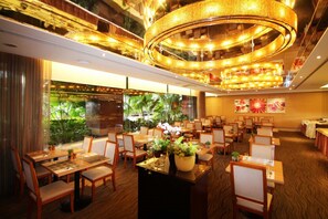 A restaurant with multiple dining tables and chairs, a central decorative light fixture, and a view of greenery through large windows. - Hotel Riverview Taipei (Taipei)