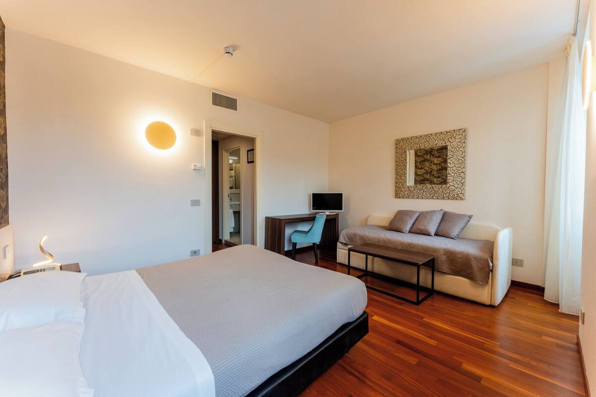A hotel room with a bed, a desk, a chair, a sofa, and a television.