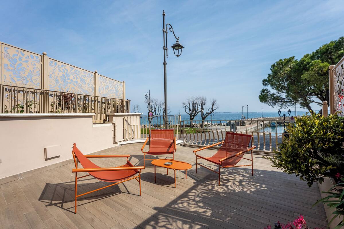A rooftop terrace with a view of the sea, equipped with orange chairs and a table.