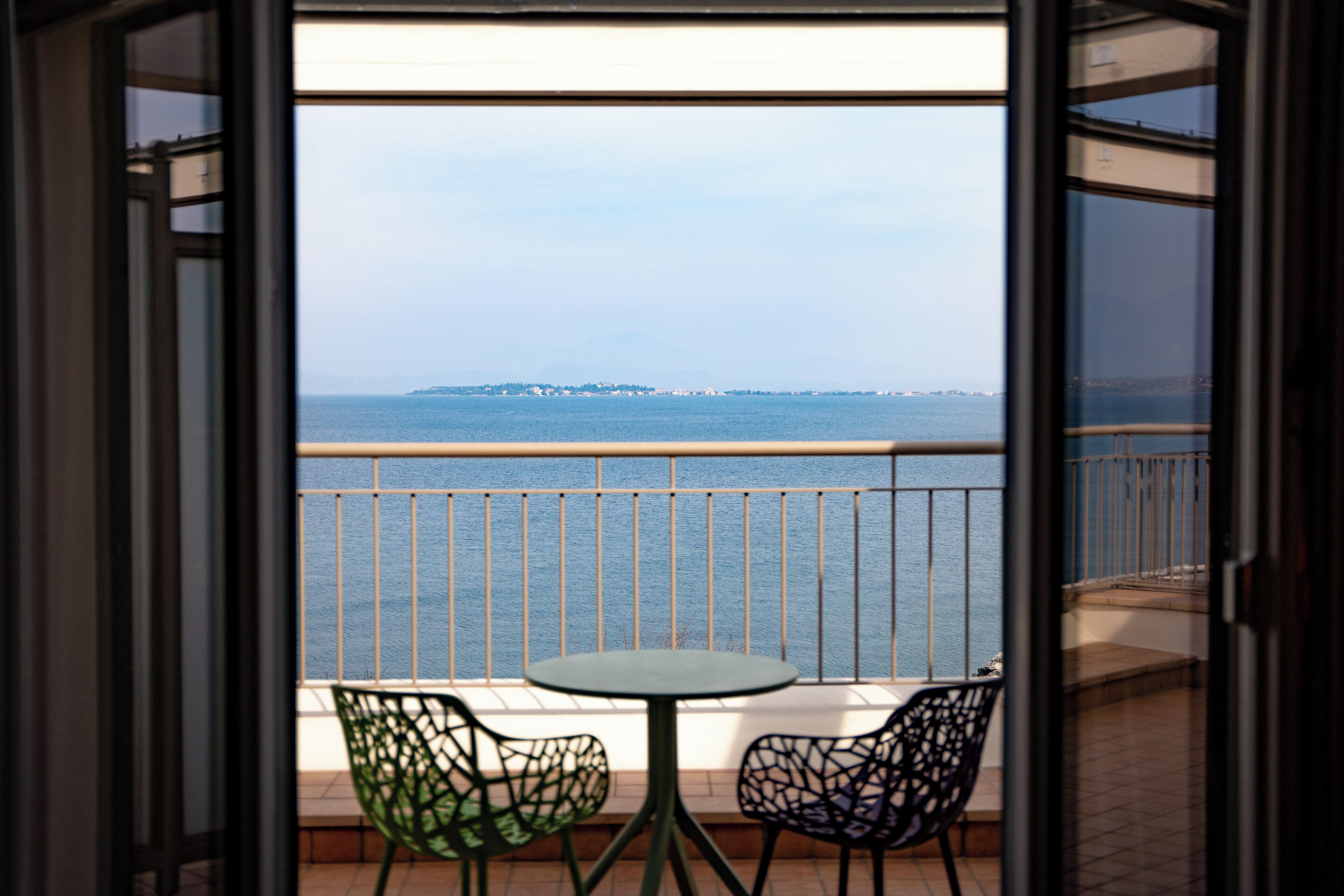 Un balcon avec deux chaises et une table, donnant sur une étendue d’eau et sur une terre lointaine.