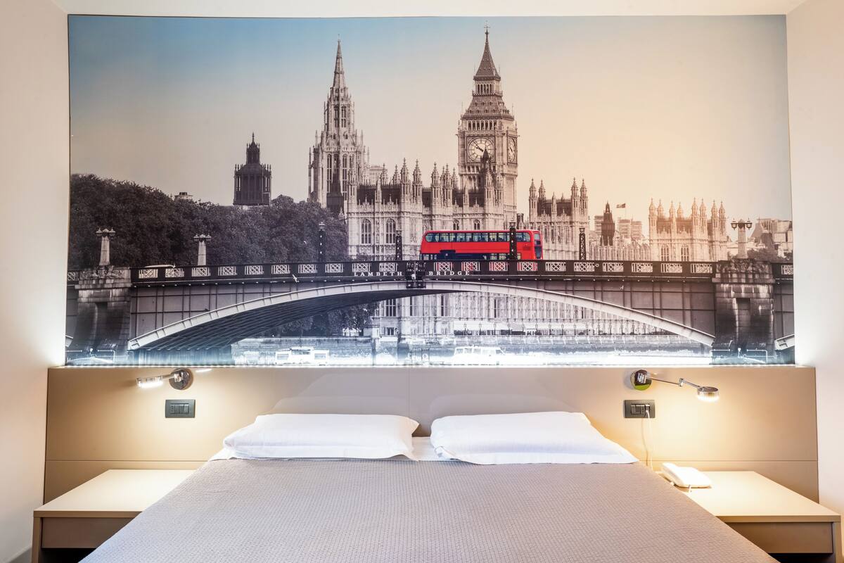 A hotel room with a large bed, two bedside tables, a nightstand, and a wall-mounted lamp.