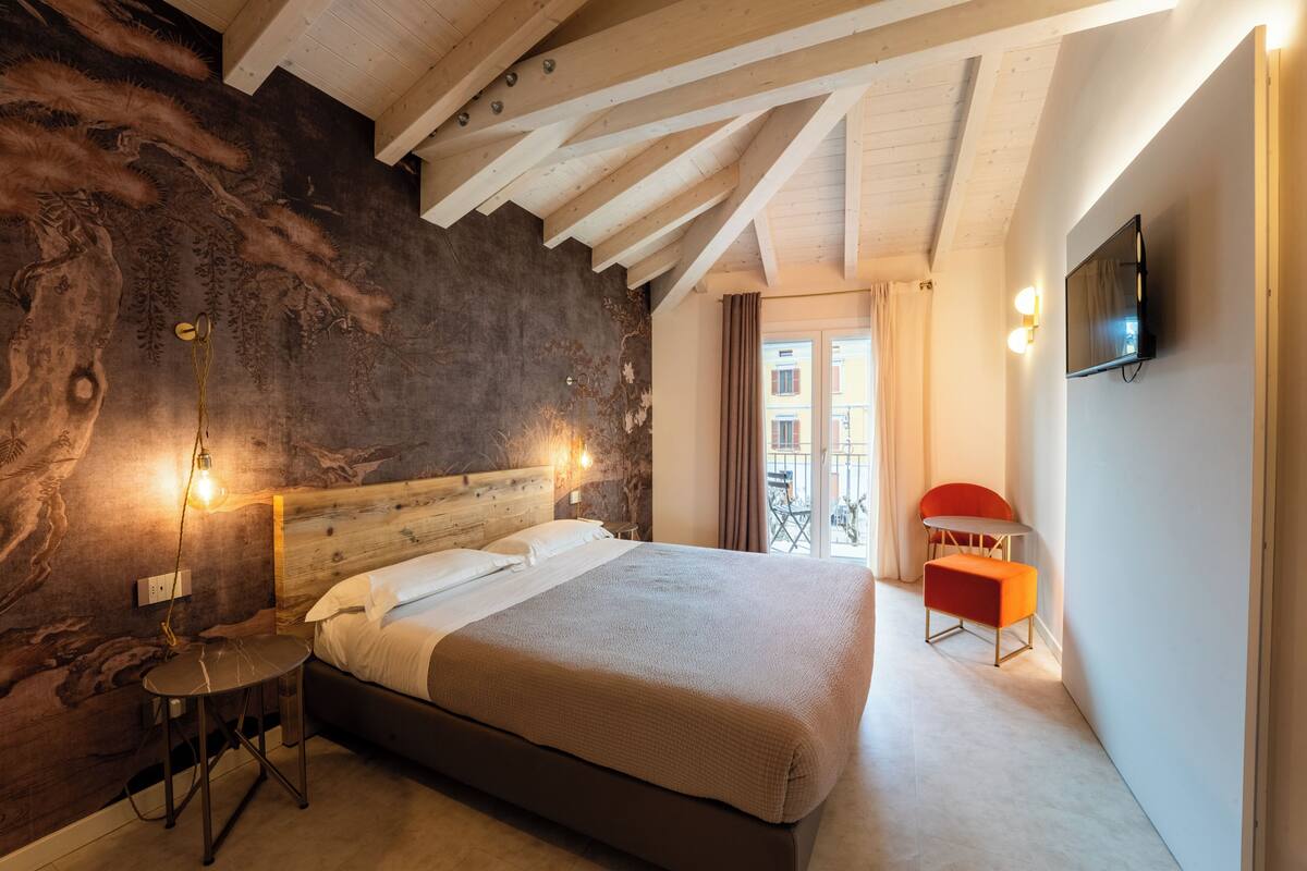 A modern bedroom with a large bed, a wooden ceiling, a stone wall, and a TV mounted on the wall.
