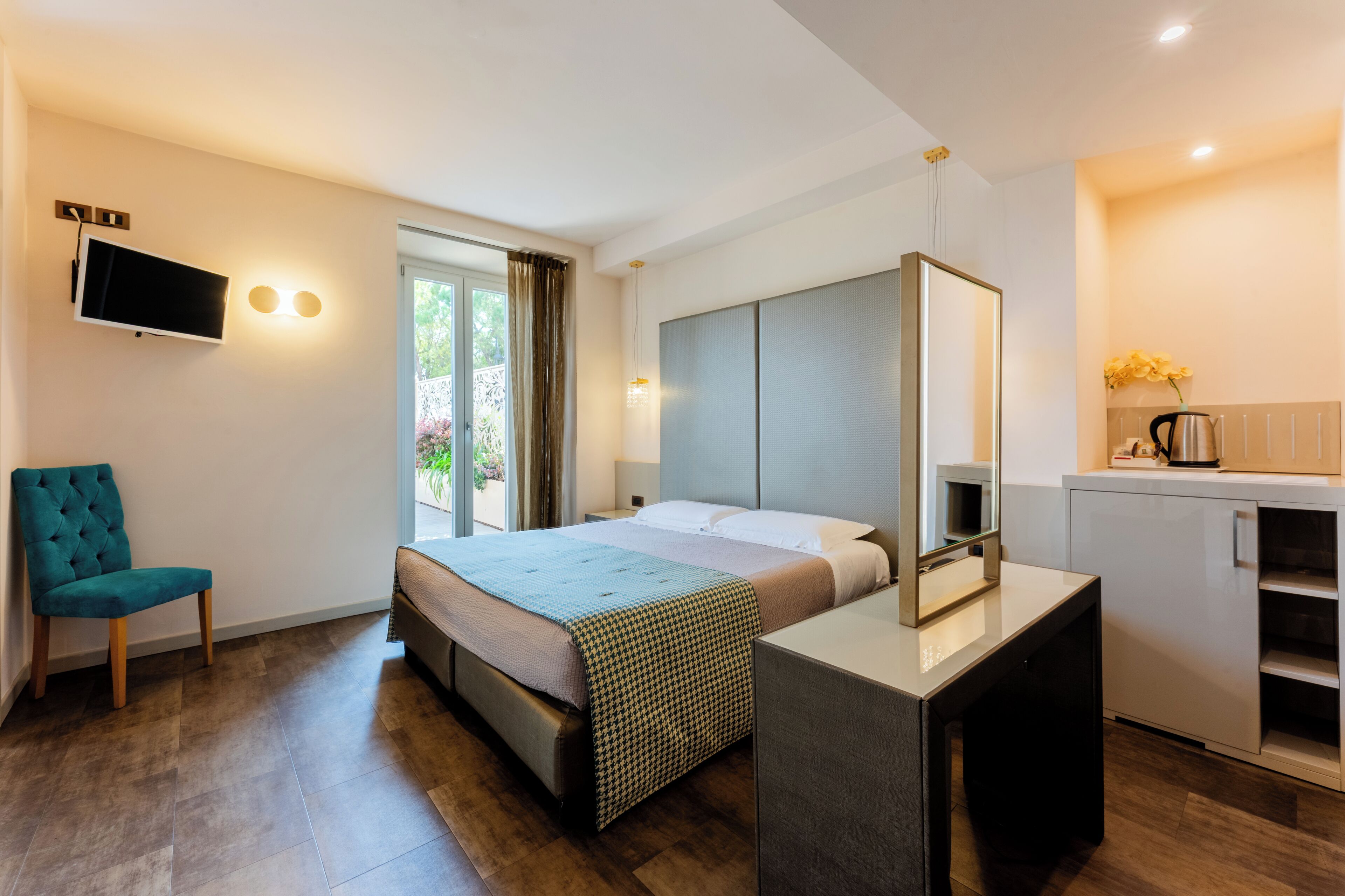 A modern hotel room with a bed, a TV, a desk, and a kitchenette.