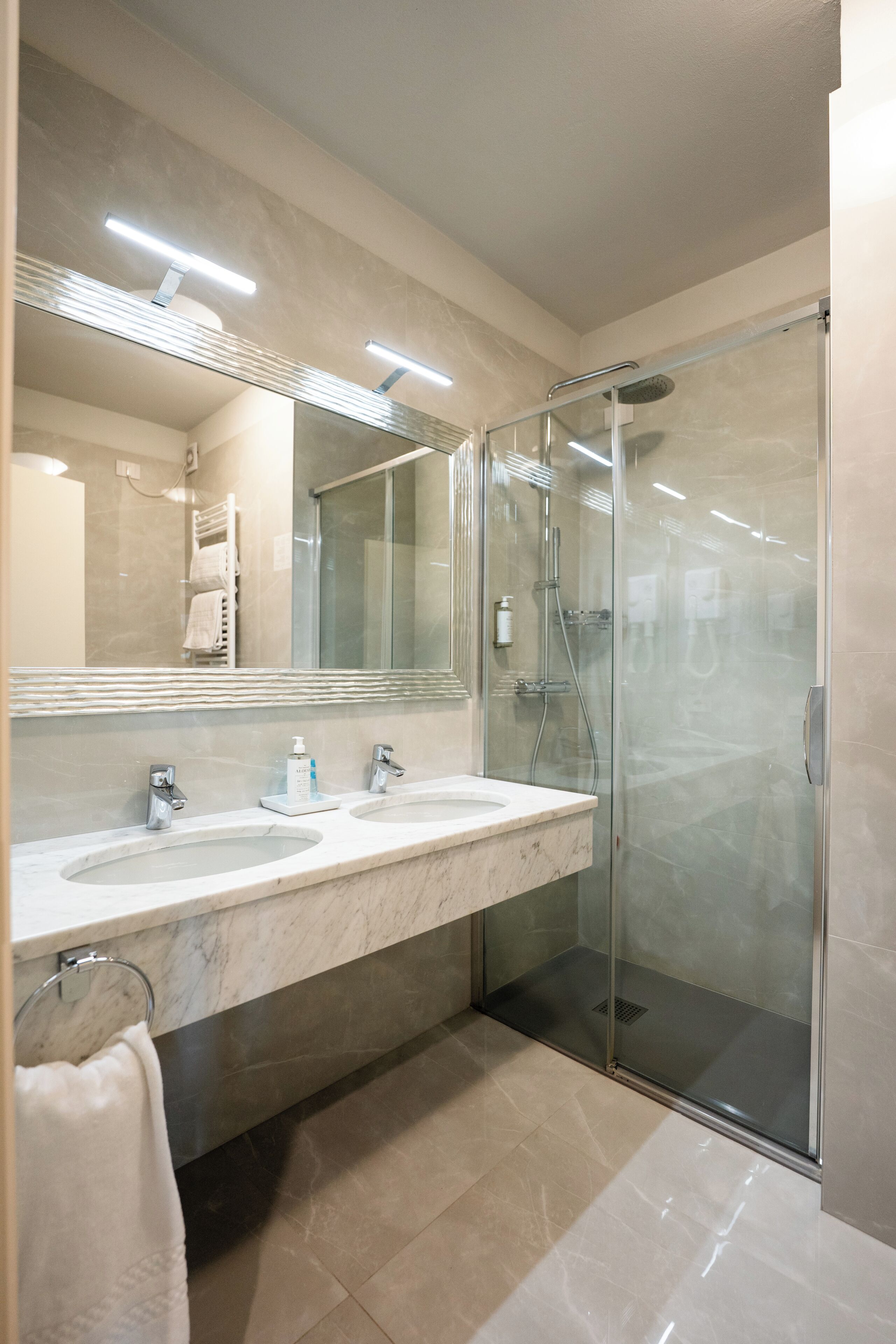 A modern bathroom with two sinks, a glass shower enclosure, and a large mirror.