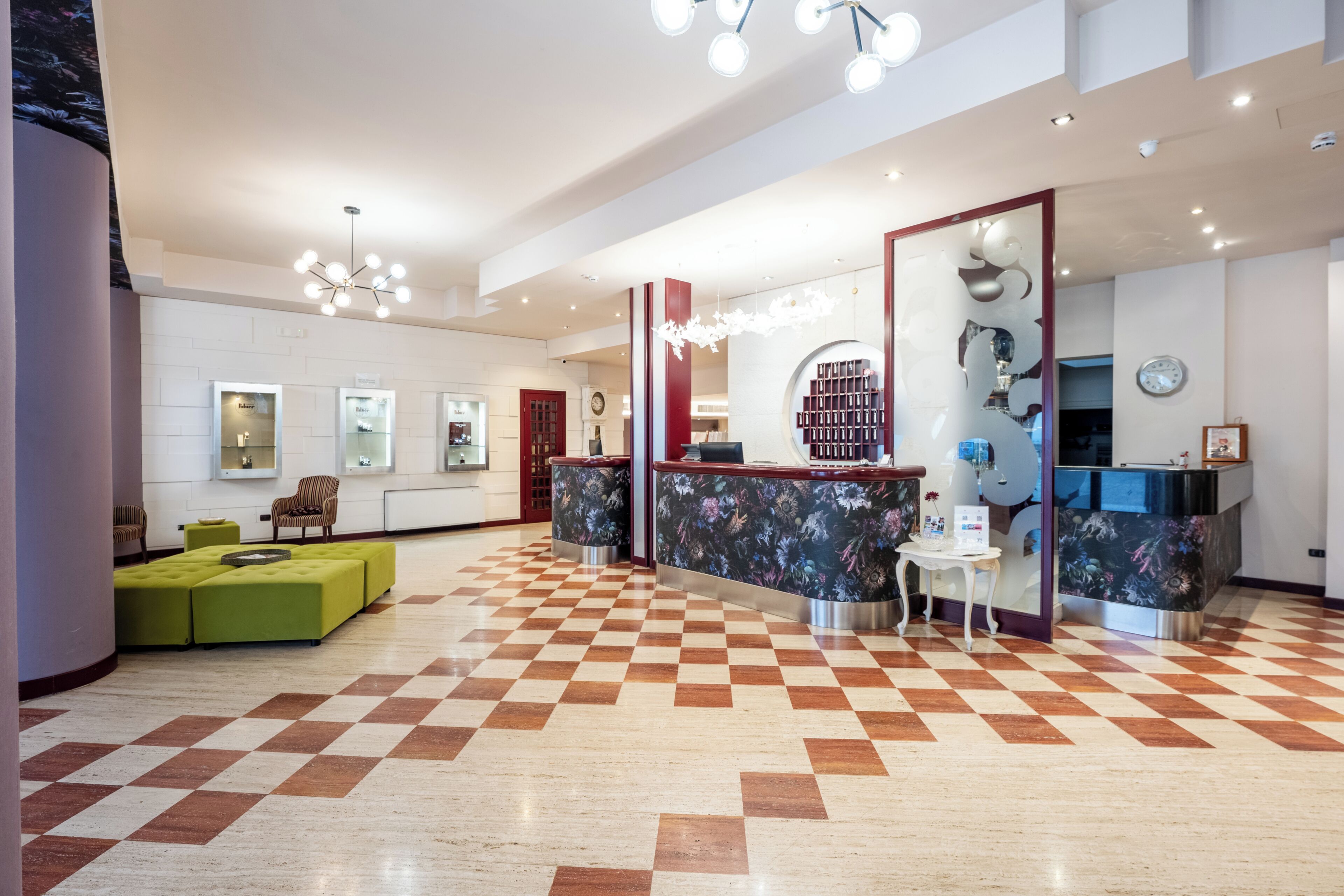 A hotel lobby with a checkered floor, a reception desk, a green seating area, and a large mirror.