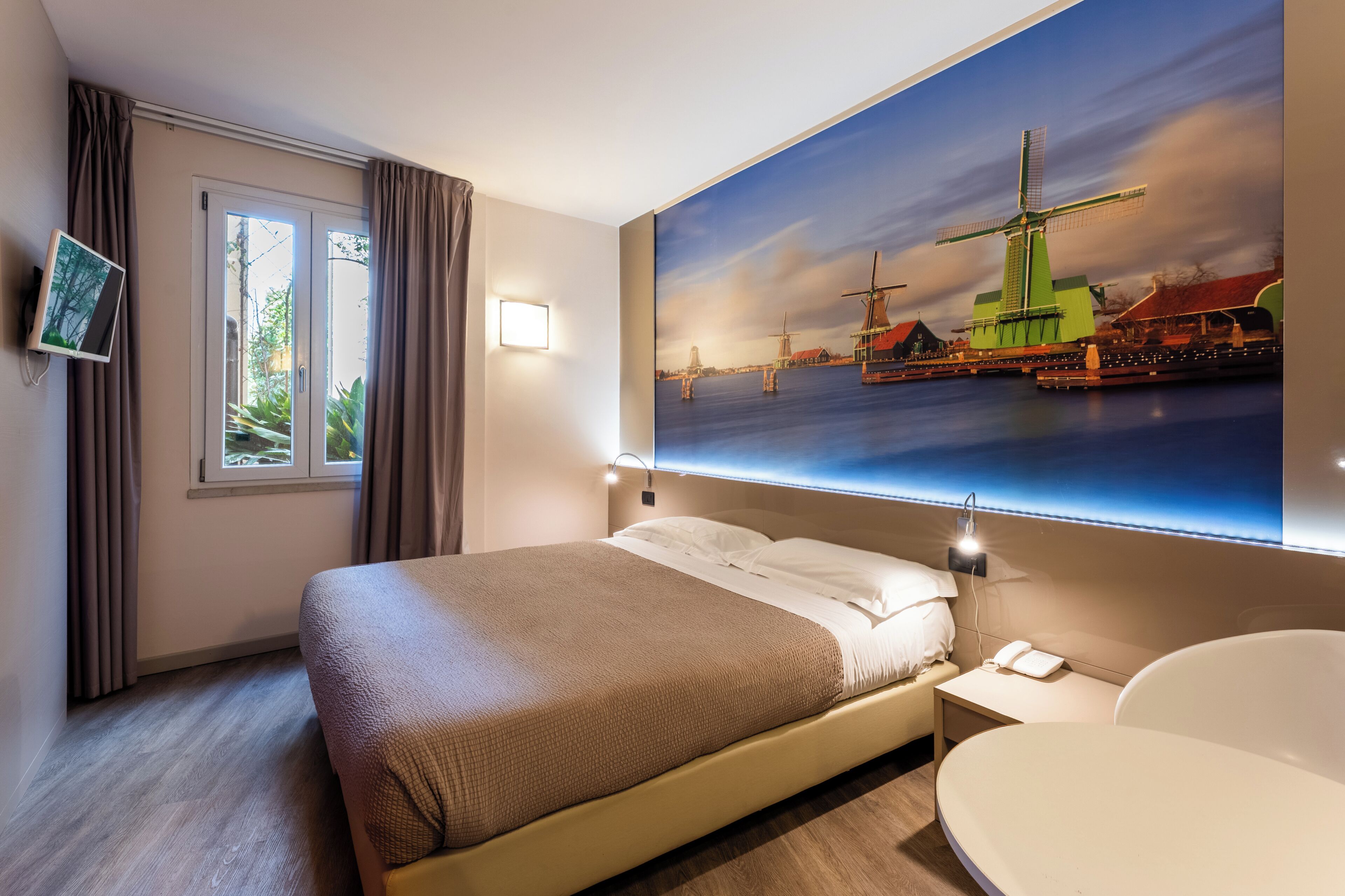 A hotel room with a bed, bedside table, and a large window.