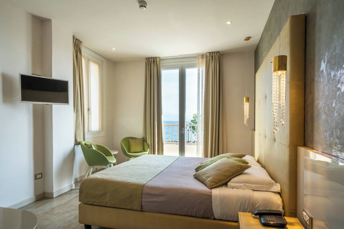 A hotel room with a bed, a chair, a TV, and a balcony with a view.