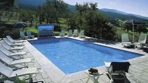 A rectangular pool with lounge chairs and umbrellas, surrounded by greenery and mountains. - Panoramahotel Post (Bressanone)