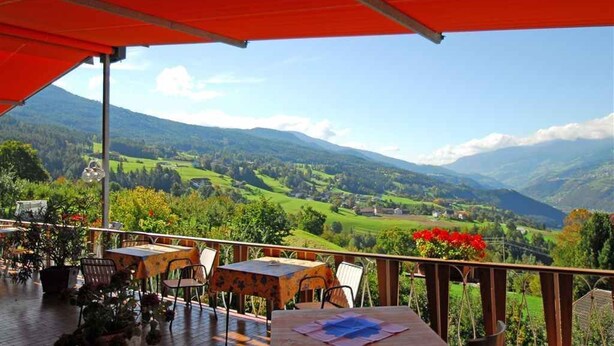 An outdoor terrace with tables and chairs, overlooking a scenic valley with mountains and greenery. - Panoramahotel Post (Bressanone)