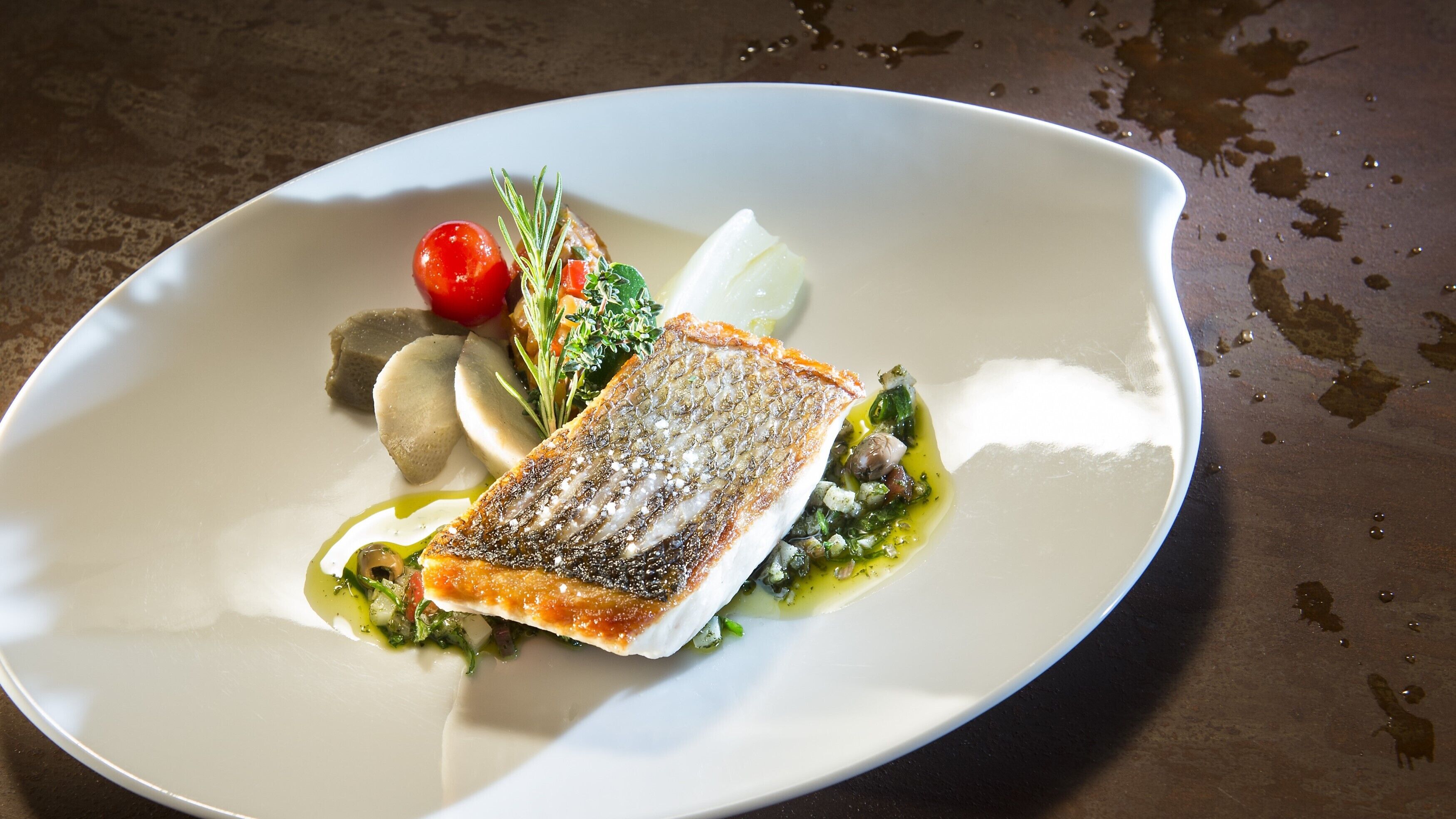 A white plate with a piece of fish, cherry tomatoes, and a sprig of rosemary.