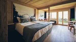 Un dormitorio de cabaña de madera con una cama grande, un cuadro de un paisaje montañoso en la pared y un ventanal corredero al exterior.