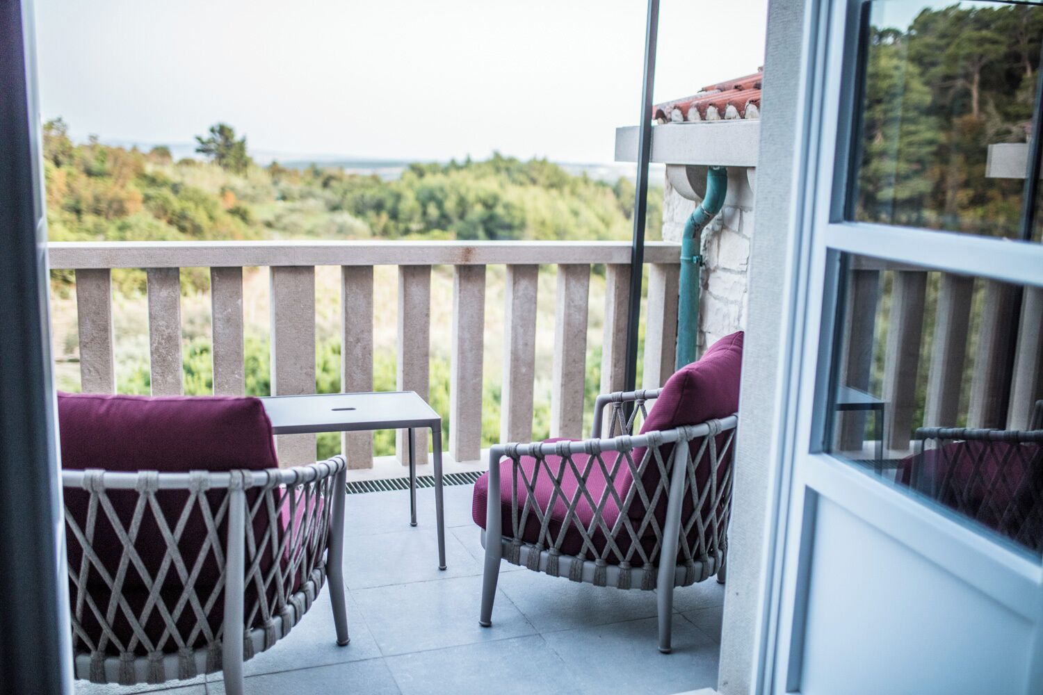 Ein Balkon mit Korbstühlen und einem Tisch, Blick ins Grüne und ein Gebäudefassaden.