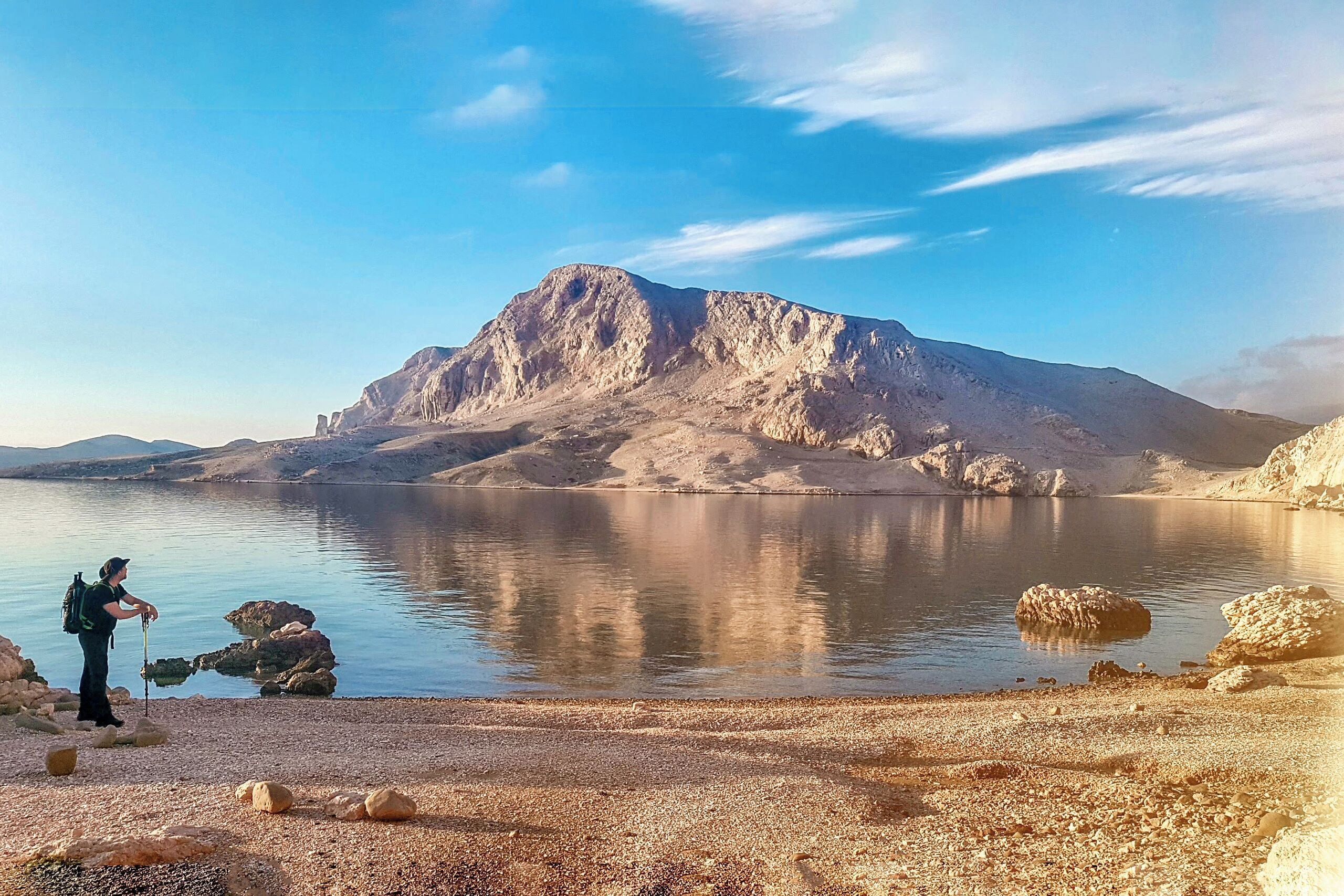 A person standing by a calm lake with a mountain in the background.