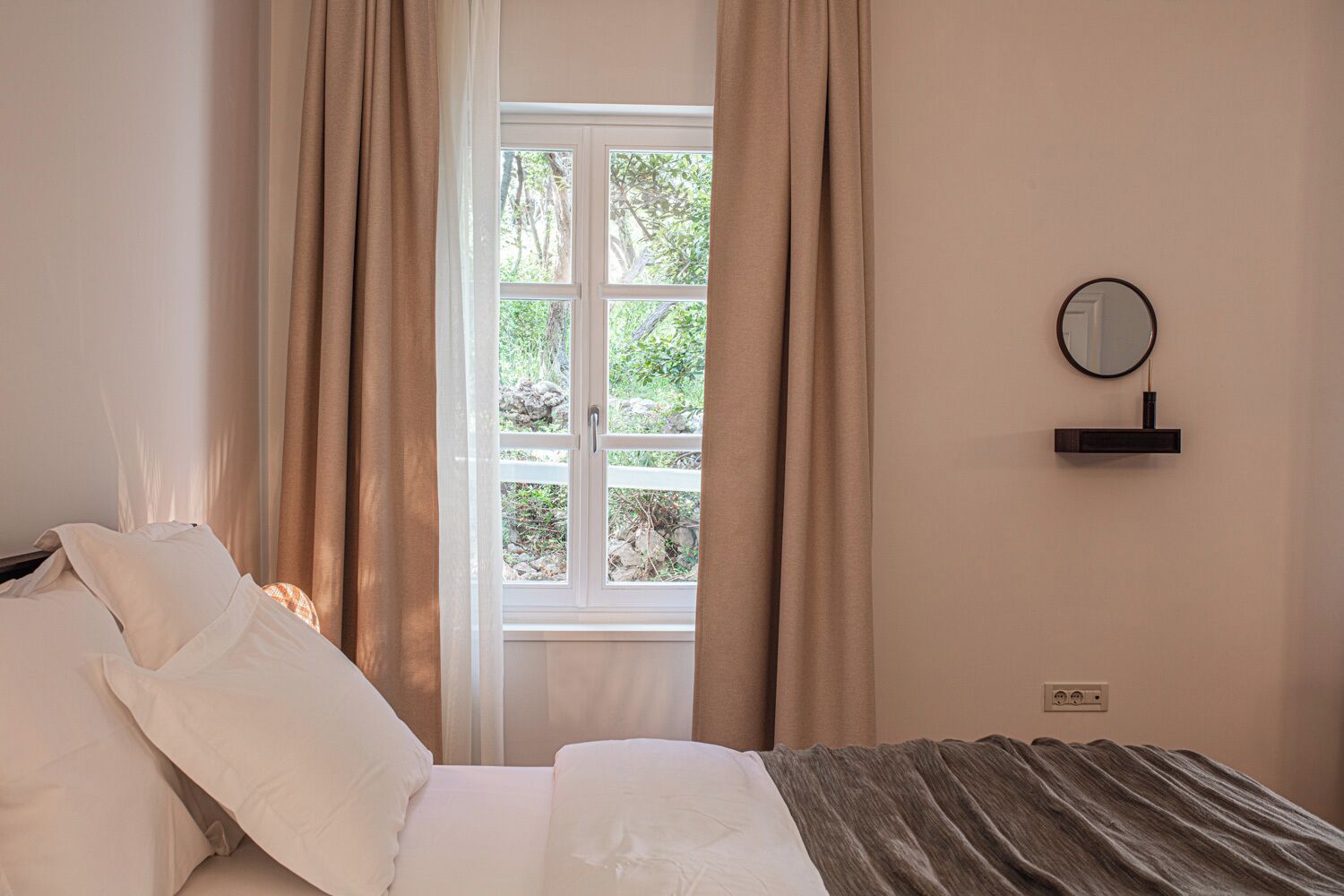 A bedroom with a bed, curtains, a window, and a wall-mounted mirror.