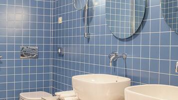Un baño con paredes de azulejos azules, dos lavamanos, un inodoro y un espejo.