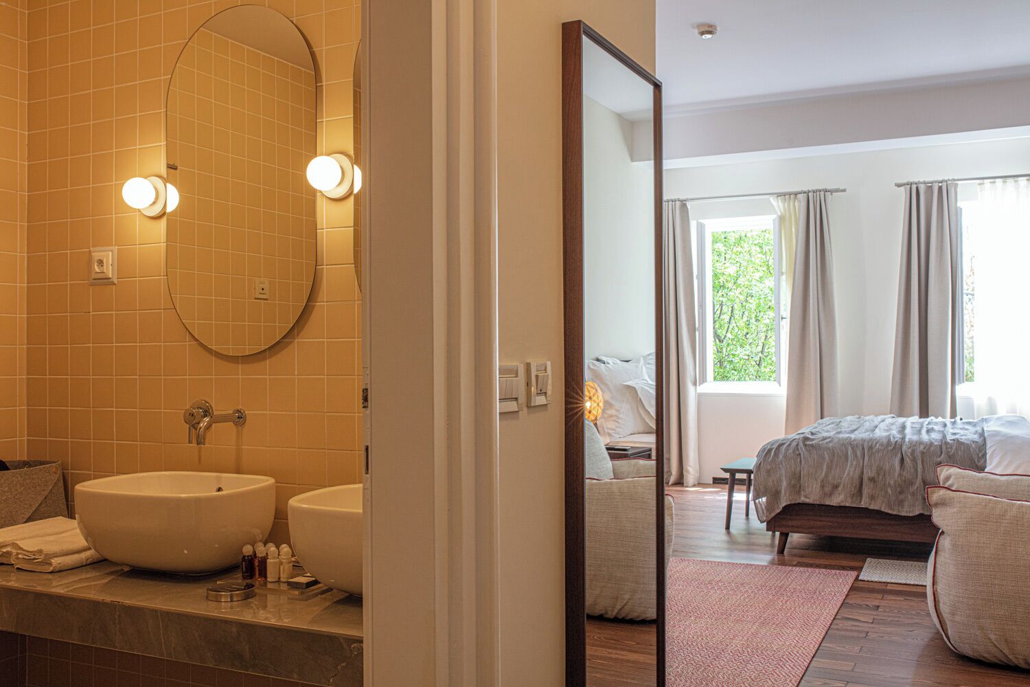 A bathroom with a large oval mirror, two sinks, and a vanity with toiletries.
