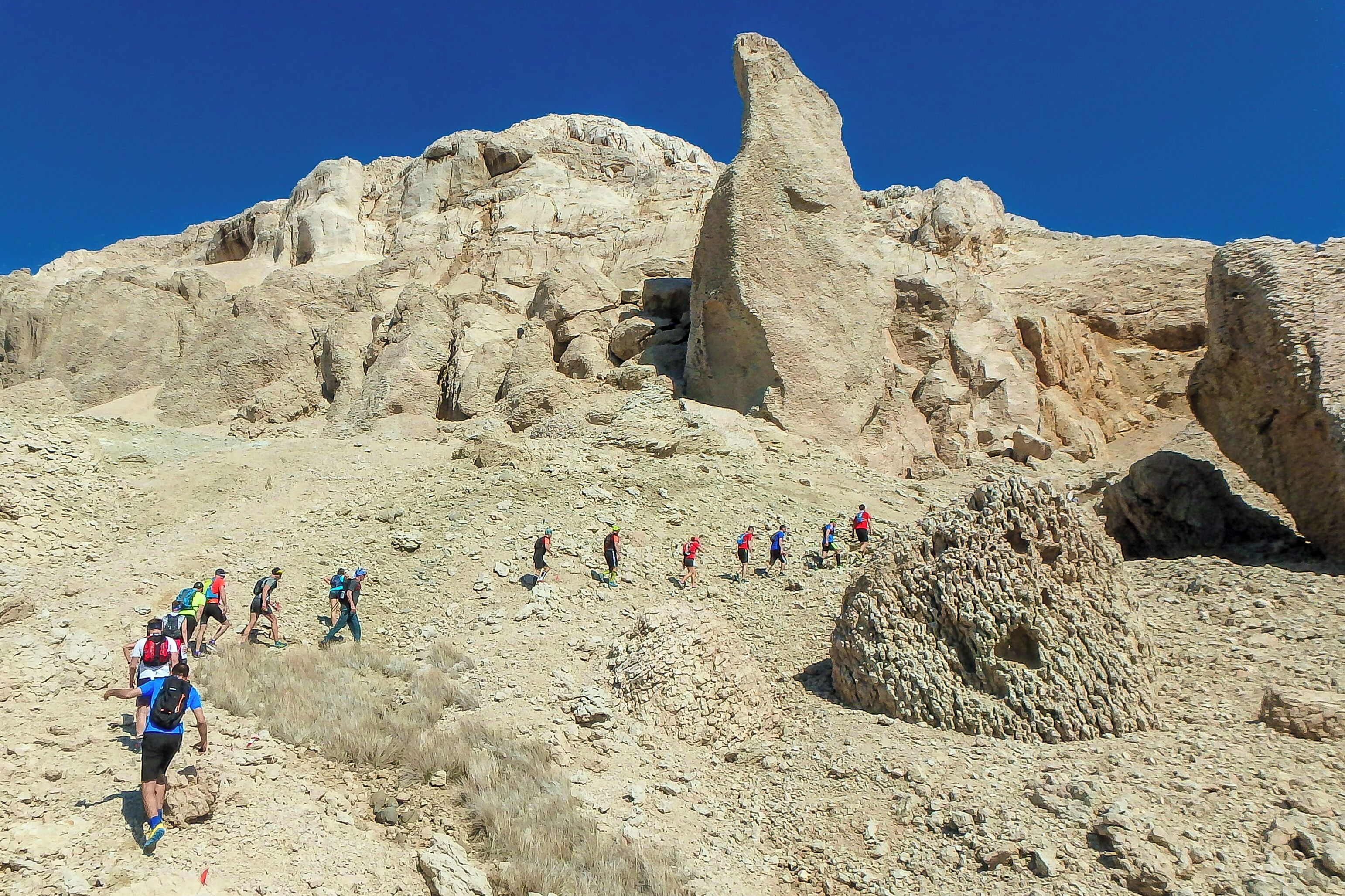 Un grupo de excursionistas en un sendero pedregoso con una gran formación rocosa al fondo.