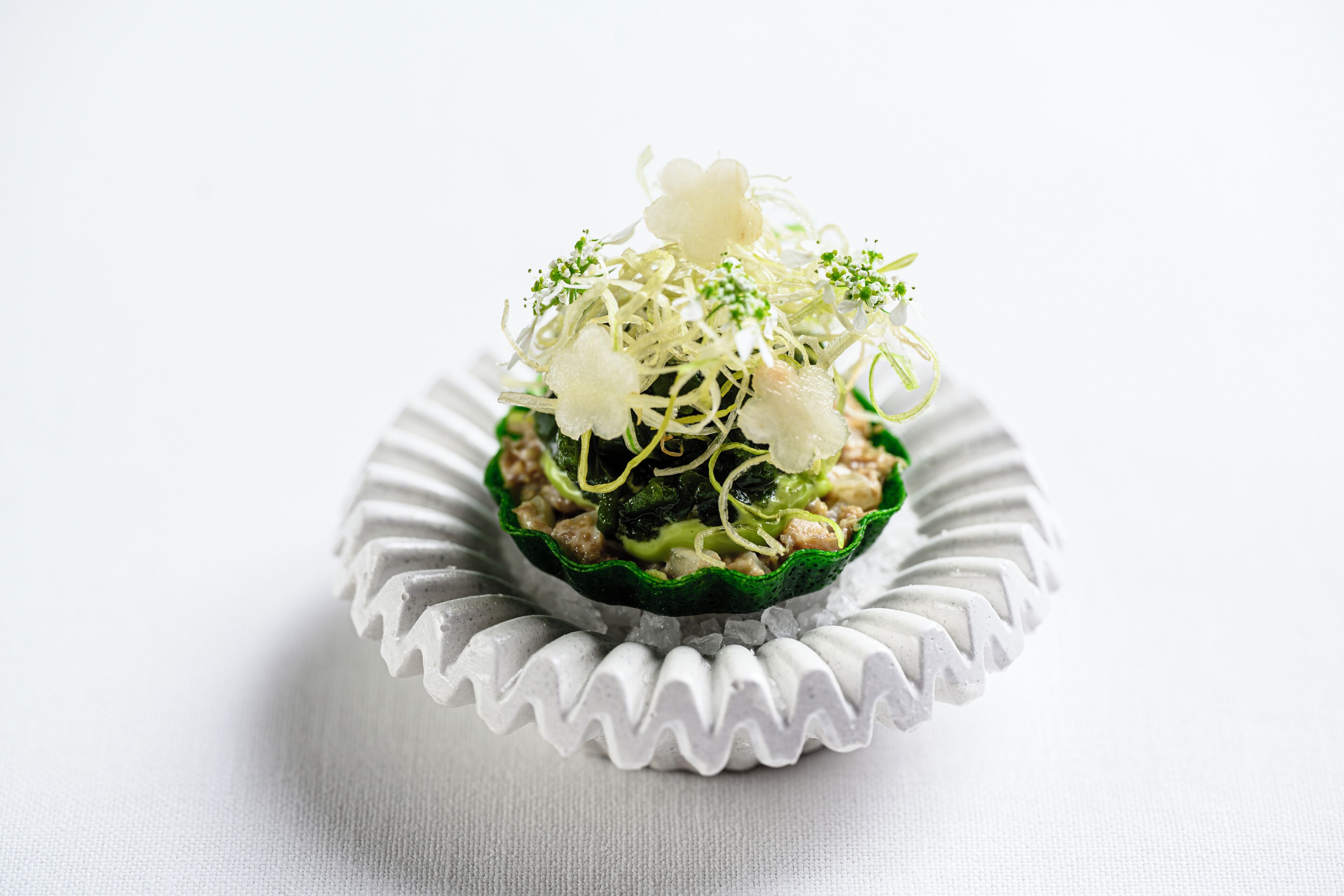 En cupcake med ett grönt pappersfodral och ett dekorativt strössel, placerad på en vit tallrik.