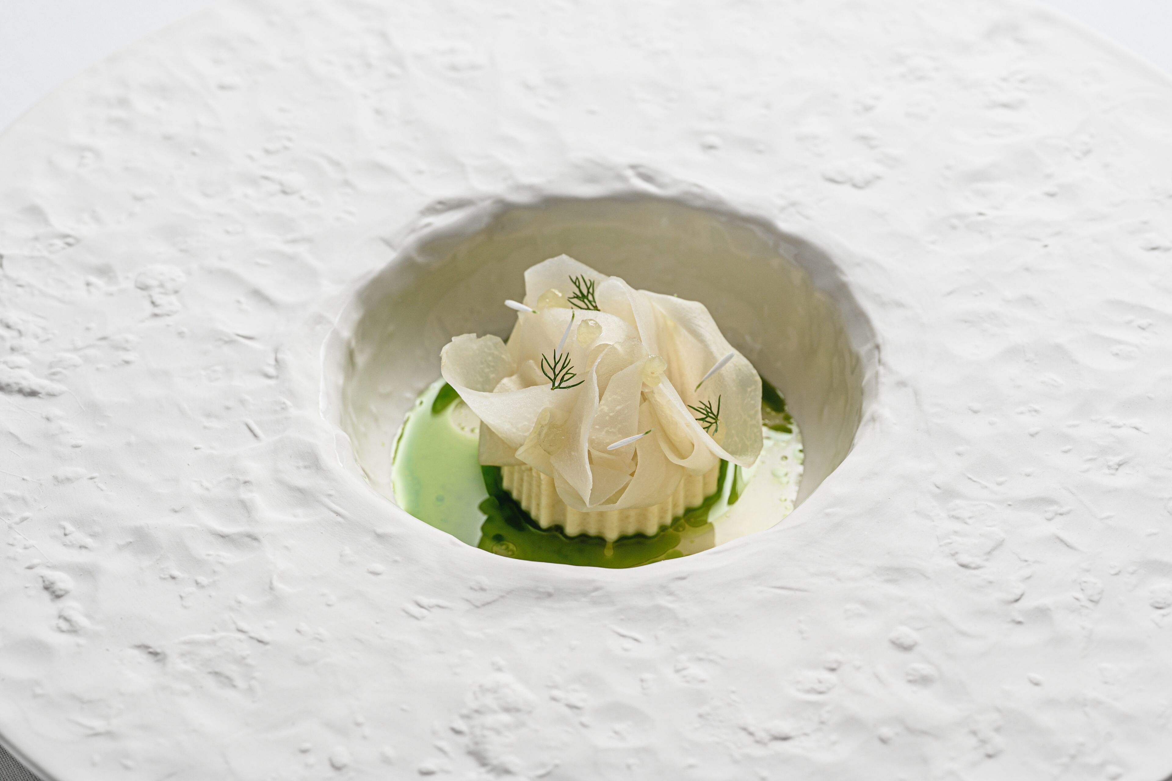 Un postre blanco en un bol con salsa verde y adorno de eneldo.