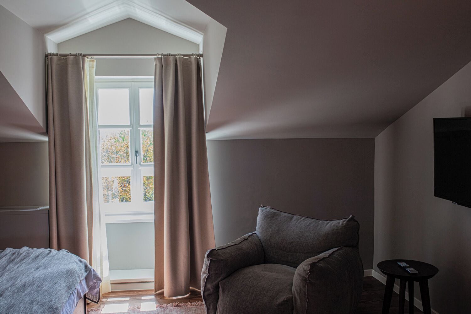 A room with a window, a chair, a bed, and a TV.