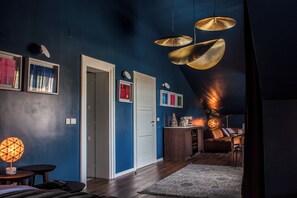 A room with a dark blue wall, a wooden floor, a white door, and a ceiling with three hanging lamps. - Hotel Boskinac (Novalja)
