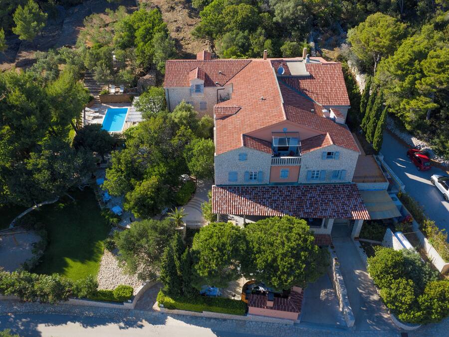 Vista aérea de una villa con piscina, rodeada de árboles y un camino de piedra.