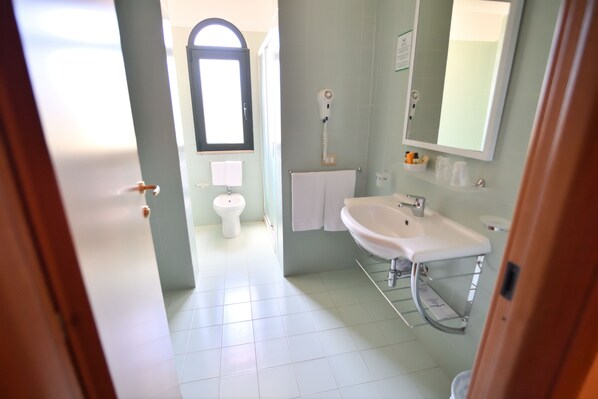 Un baño con lavamanos blanco, espejo y toallero.