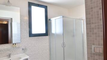 Un baño con cabina de ducha de vidrio, lavamanos y espejo.