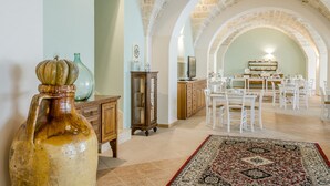 A spacious dining area with white chairs and a table, a large vase, and a cabinet. - Laurito Resort & Spa (Oria)