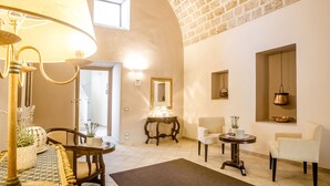 A spacious living area with a high arched ceiling, a dining table with chairs, a sofa, and a small side table with a lamp. - Laurito Resort & Spa (Oria)