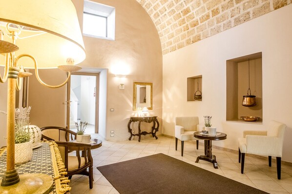 A spacious living area with a high arched ceiling, a dining table with chairs, a sofa, and a small side table with a lamp. - Laurito Resort & Spa (Oria)