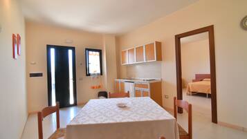 Un comedor con mesa y sillas, una cocina con armarios y un dormitorio visible a través de una puerta abierta.